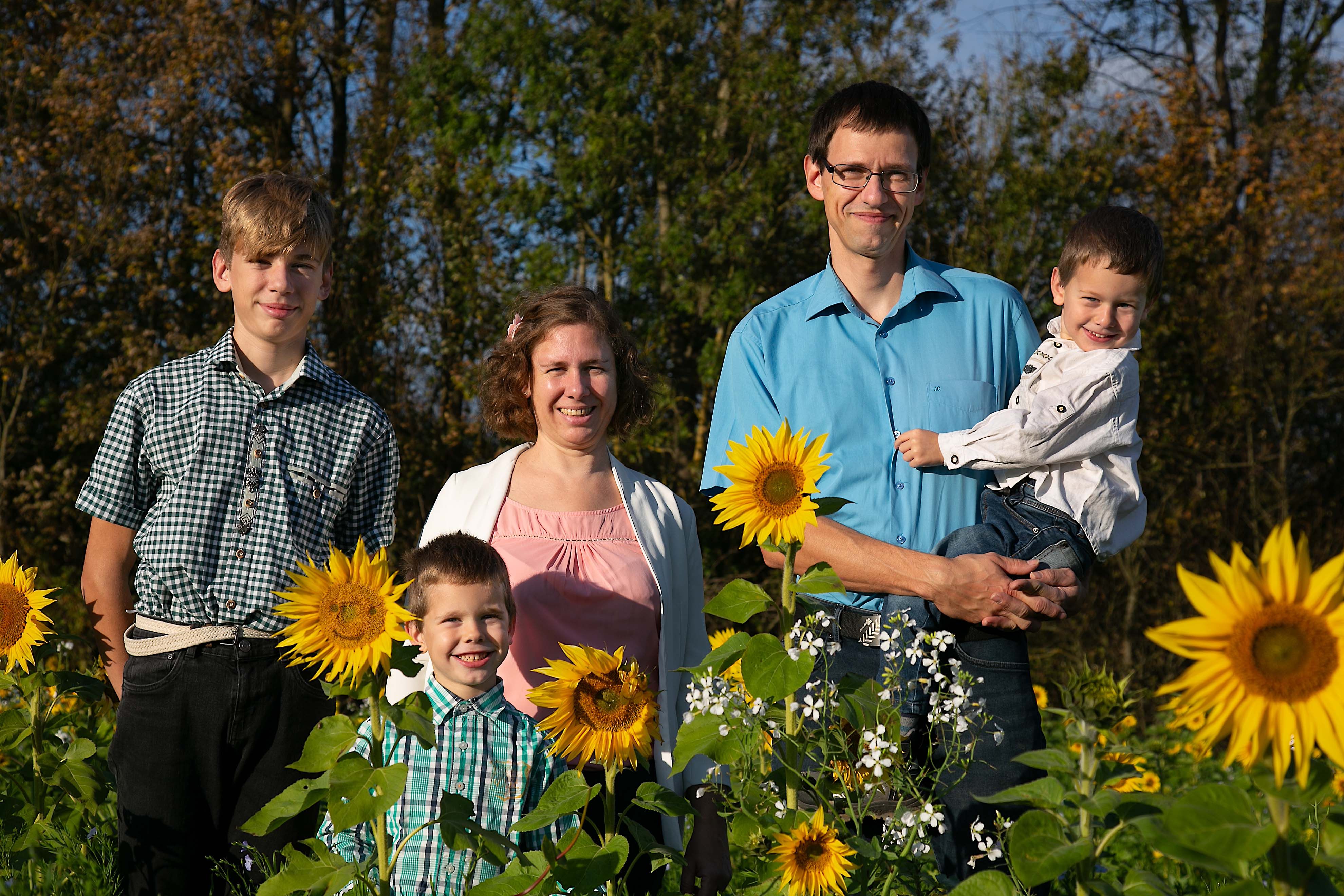 A family stands smiling in a field of sunflowers.