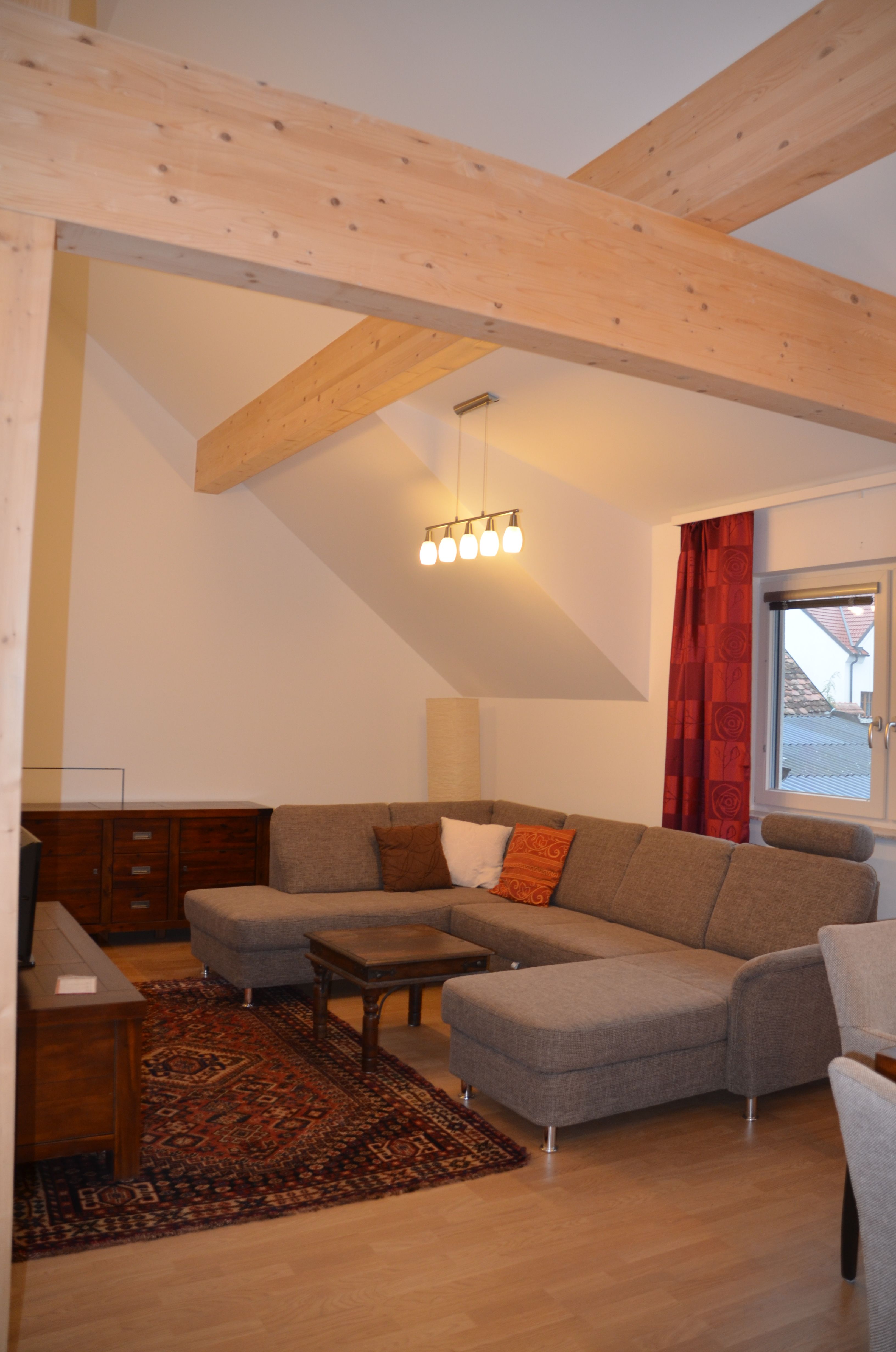 Modern living room with gray corner sofa, wooden beams, carpet and lamp.