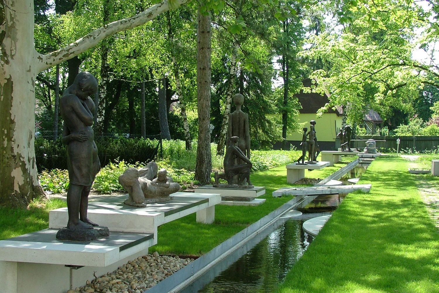 Outdoor sculptures in a green park with trees and a watercourse.