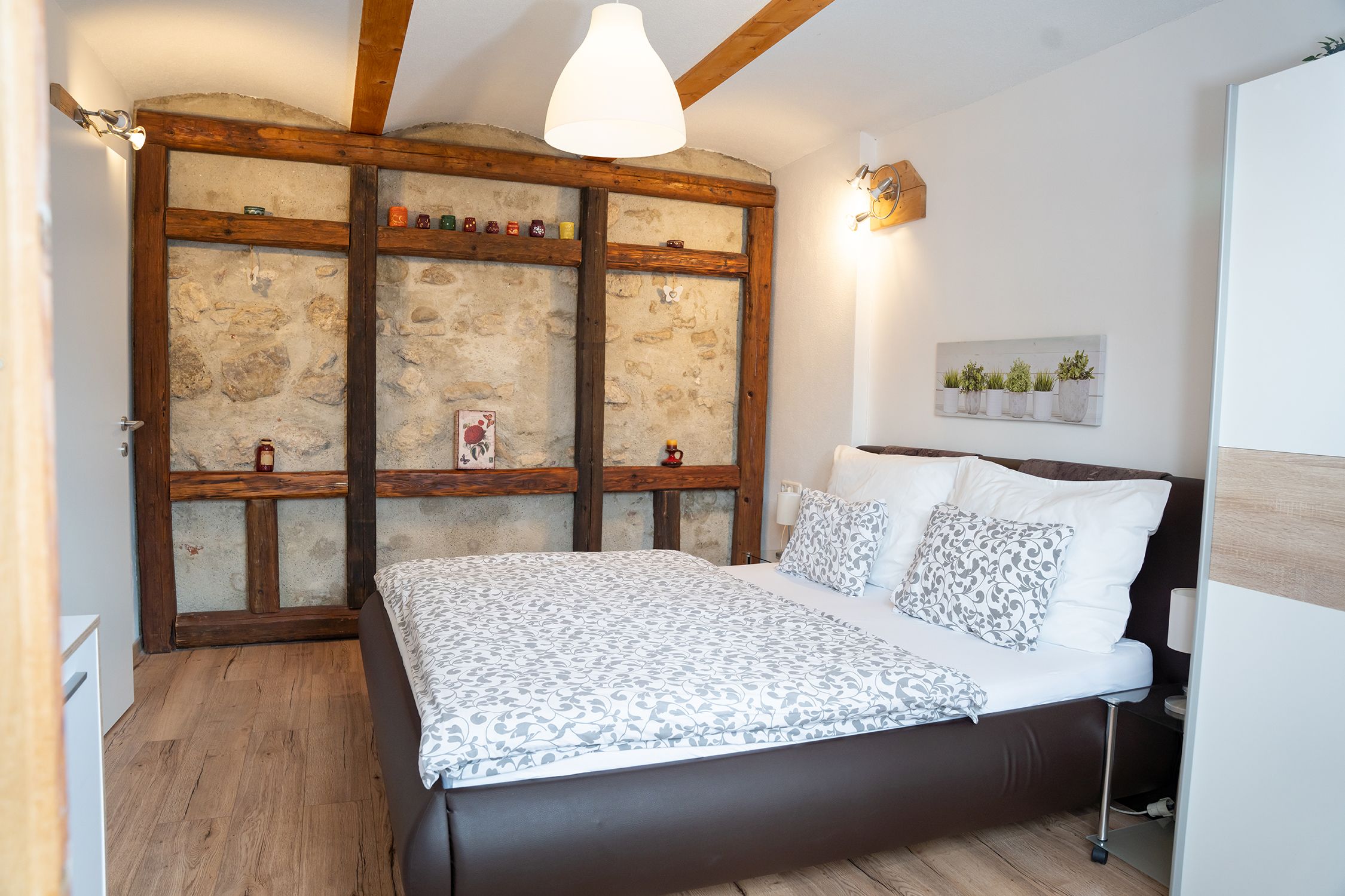 Cozy bedroom with wooden beams, stone wall and modern bed.