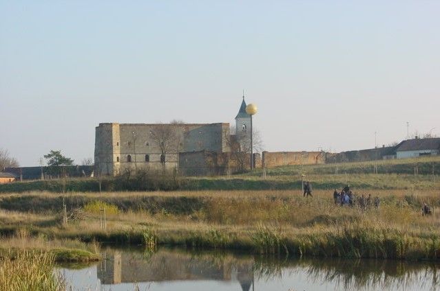 Ruin with tower and golden ball in a rural landscape with a pond in the foreground.