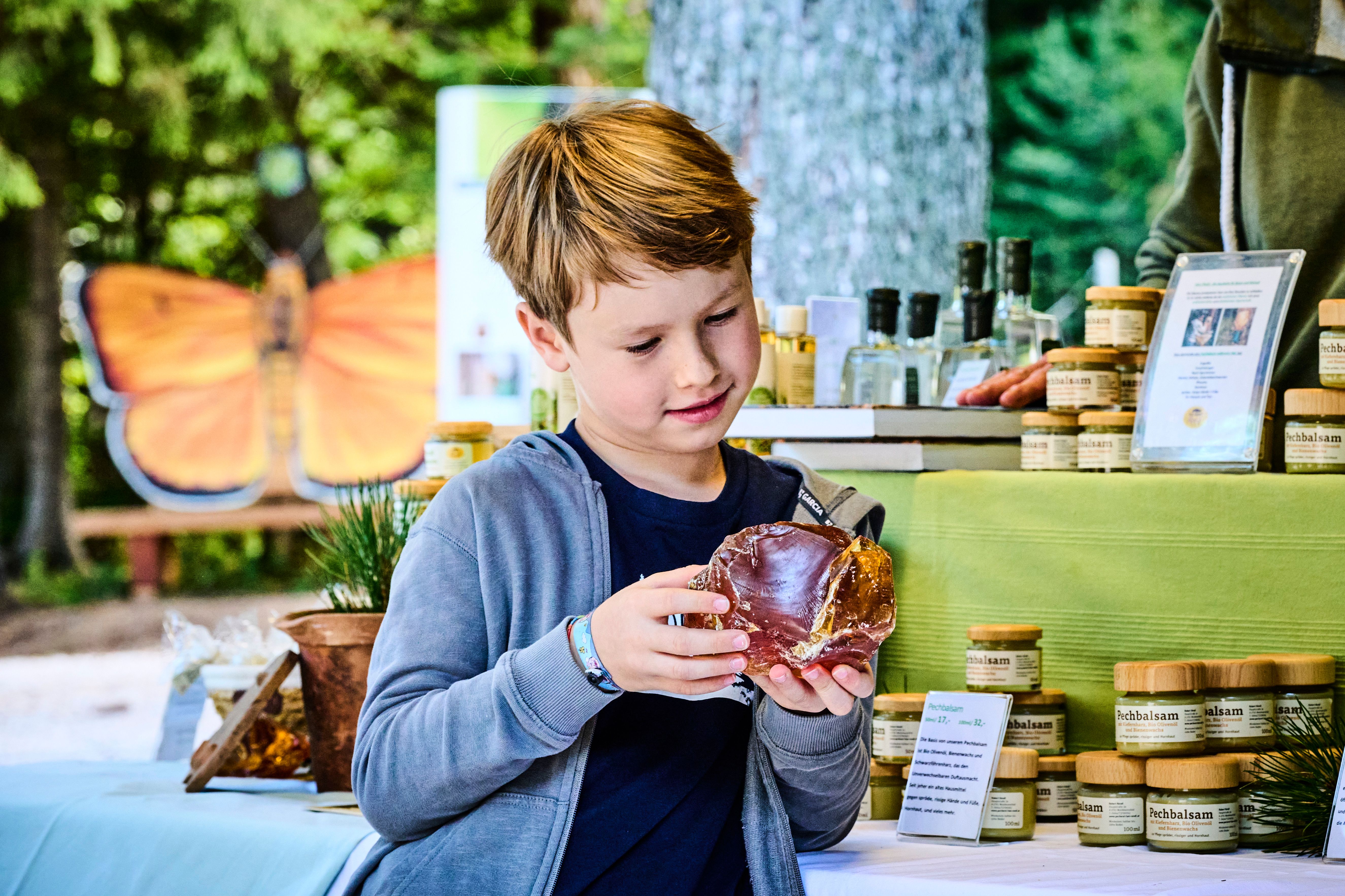 A boy looks at a large piece of resin on a market stall selling natural products.