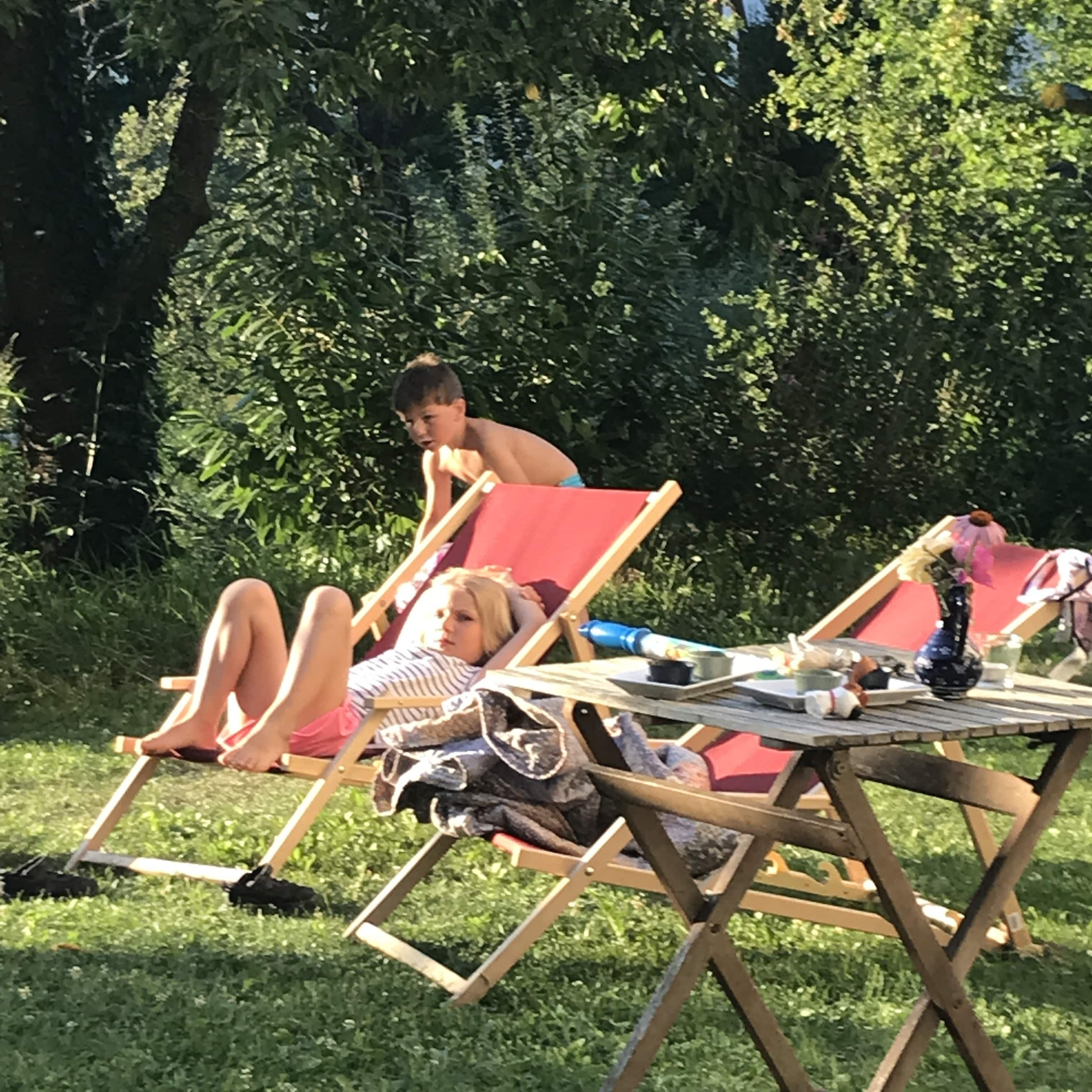 Two children relax on sun loungers in the garden.