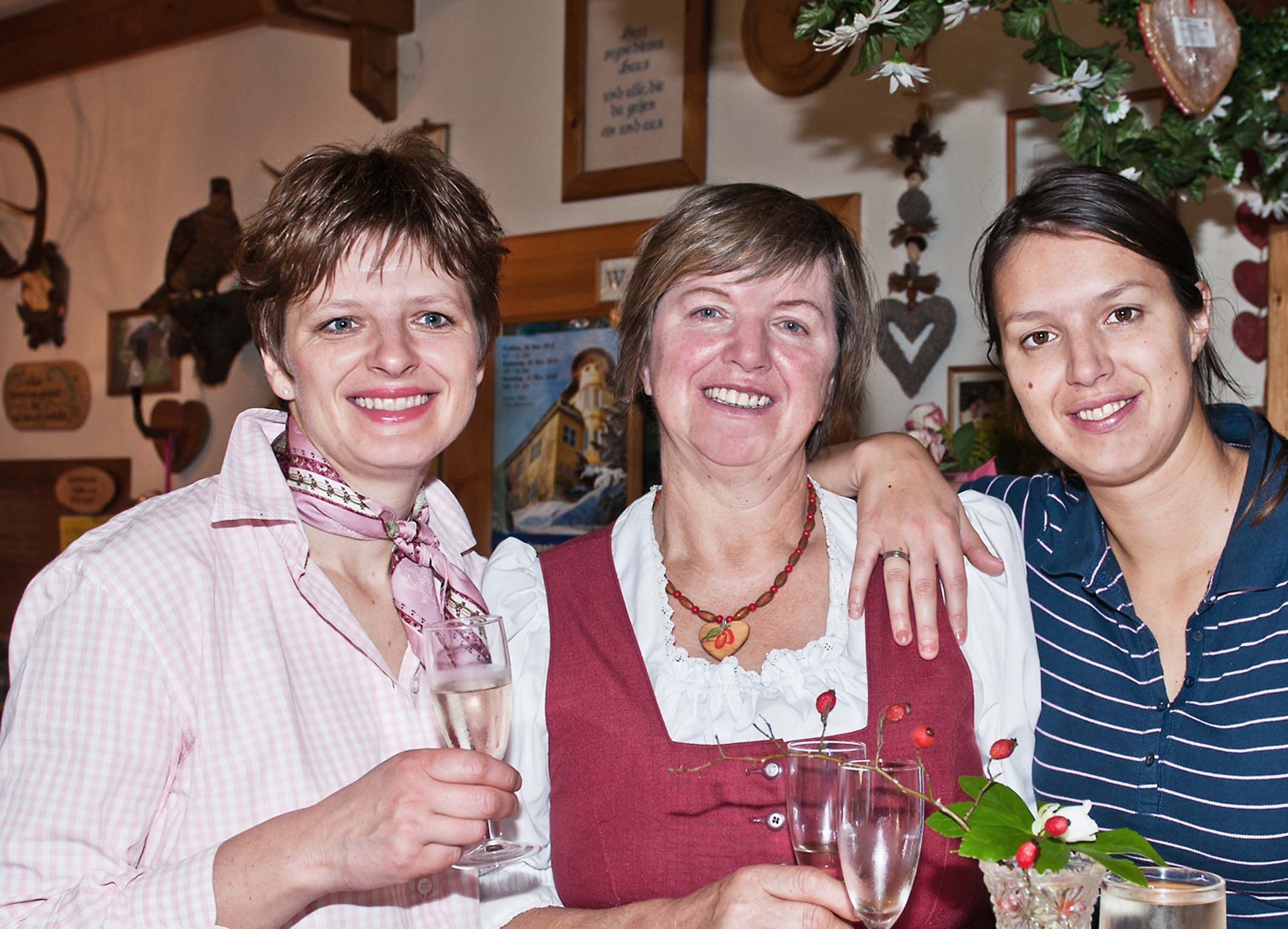 Three women smile at the camera and hold champagne glasses in their hands.