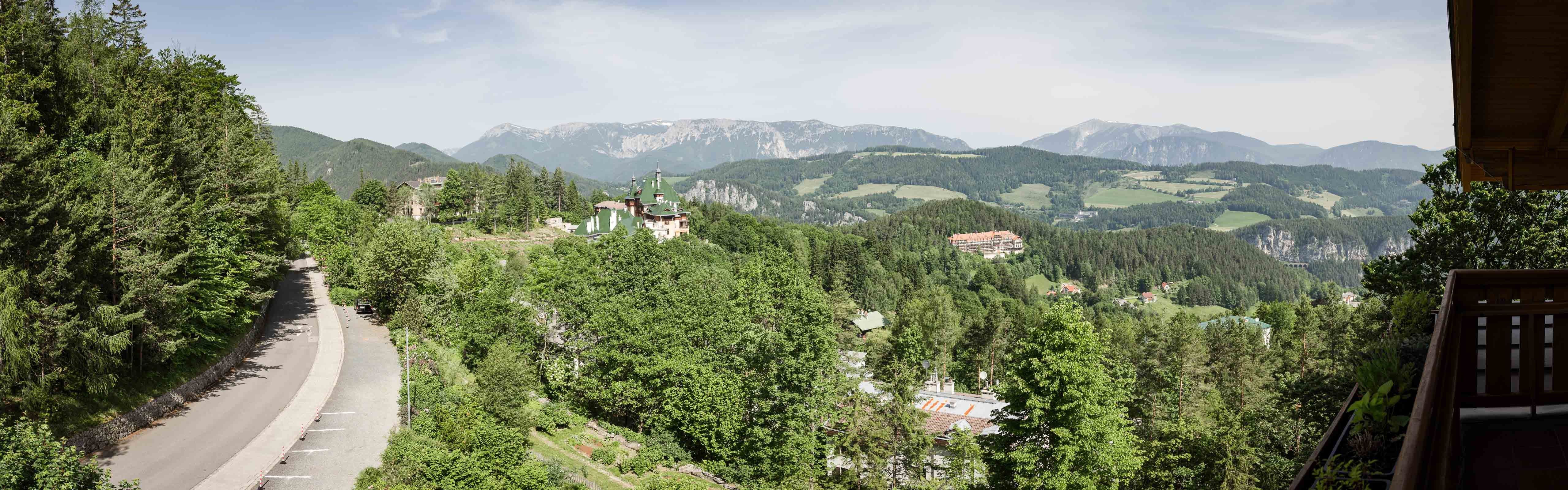Panoramic view of a mountainous landscape with forest, road and buildings.
