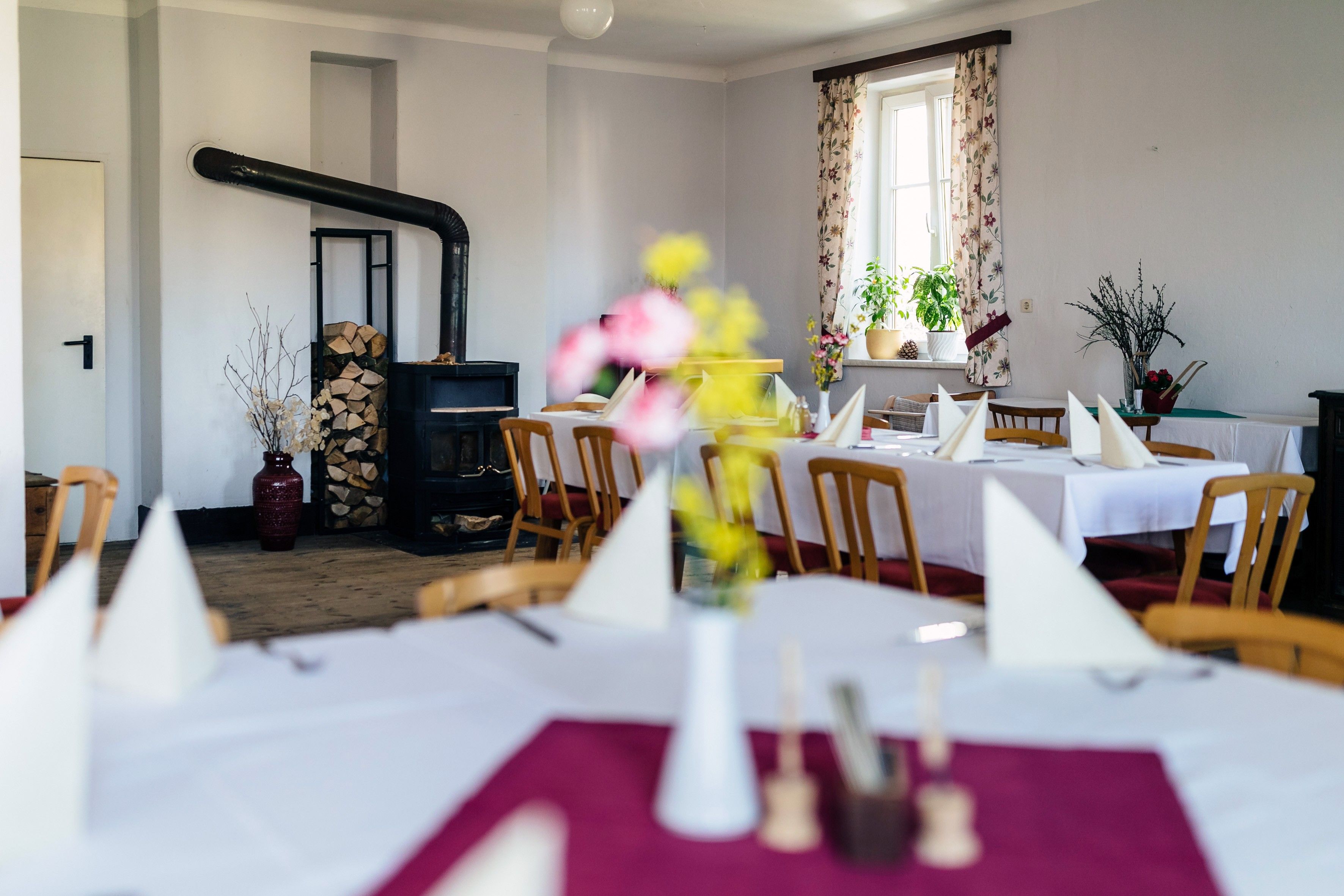 A cozy dining room with a wood-burning stove, laid tables and flowers on the tables.
