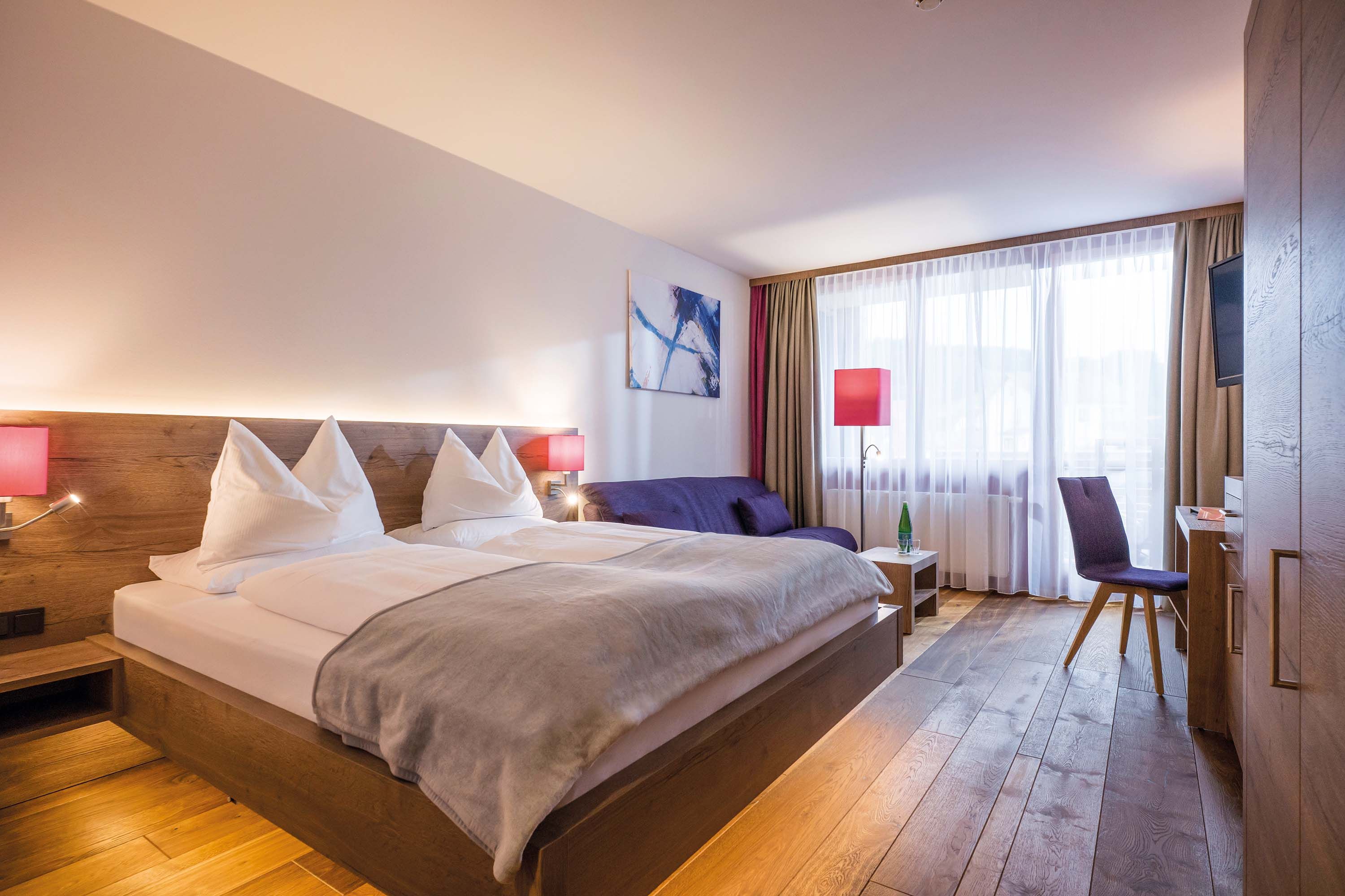 Cozy double room with wooden floor and furniture, sofa, closet, TV and red lamps.