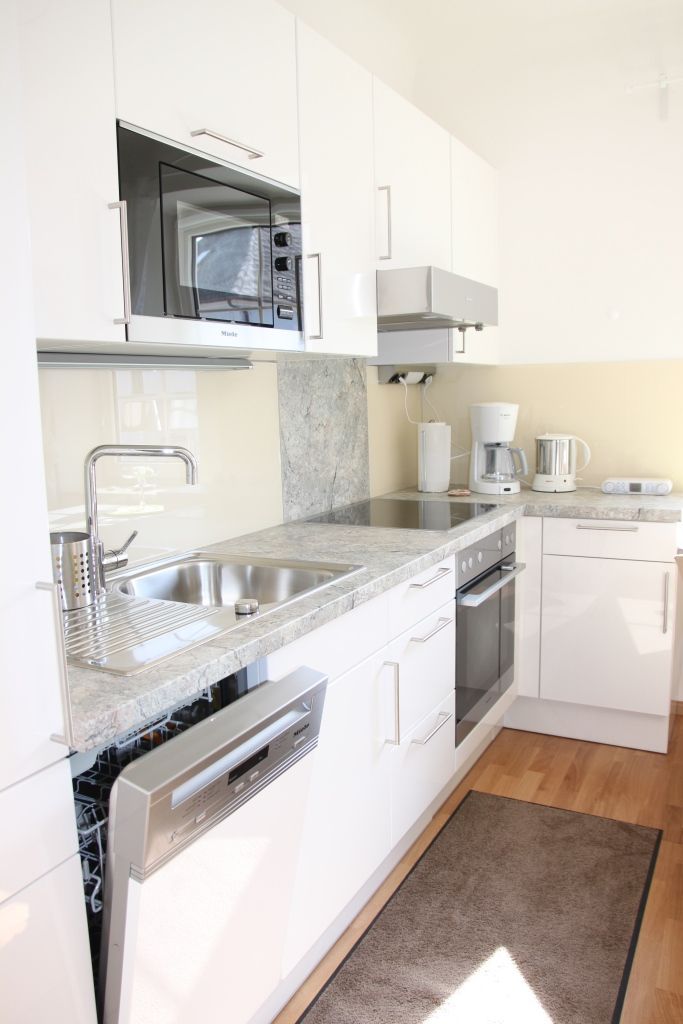 Modern kitchen with white cupboards, sink, dishwasher, microwave and coffee machine.