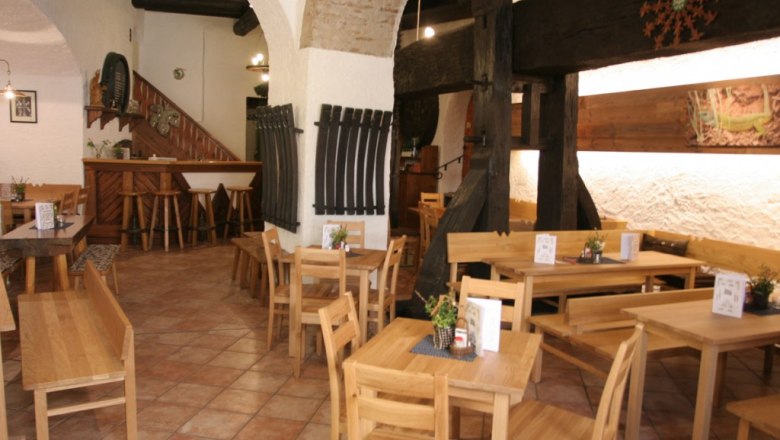 Interior view of a rustic wine tavern with wooden furniture and brick arches.