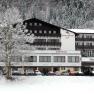 A snow-covered hotel building with the inscription 'Sporthotel' and 'Cafeteria', surrounded by snow-covered trees and parked cars.