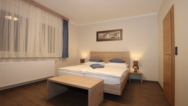 Rooms in the Pension Central, © Konrad Brandl A simply furnished room with a double bed, wooden furniture and curtains.