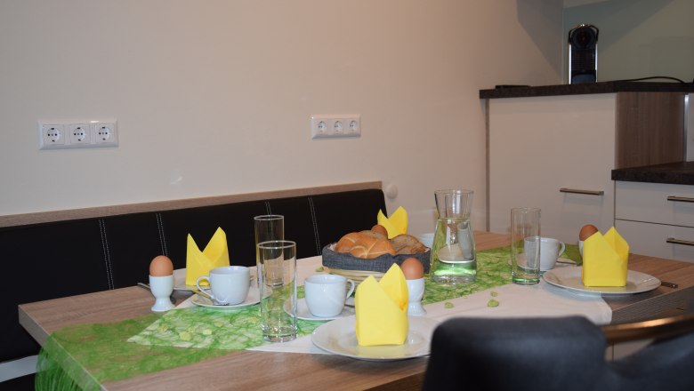 Breakfast table with bread rolls, eggs, cups and yellow napkins.