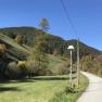 Rural road with lantern, surrounded by green hills and trees under a blue sky.
