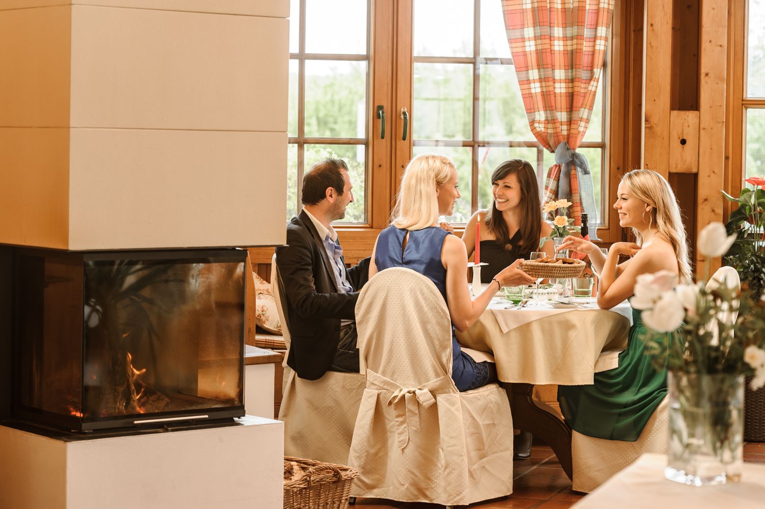Four people sit at a table in a cozy winter garden with a fireplace.