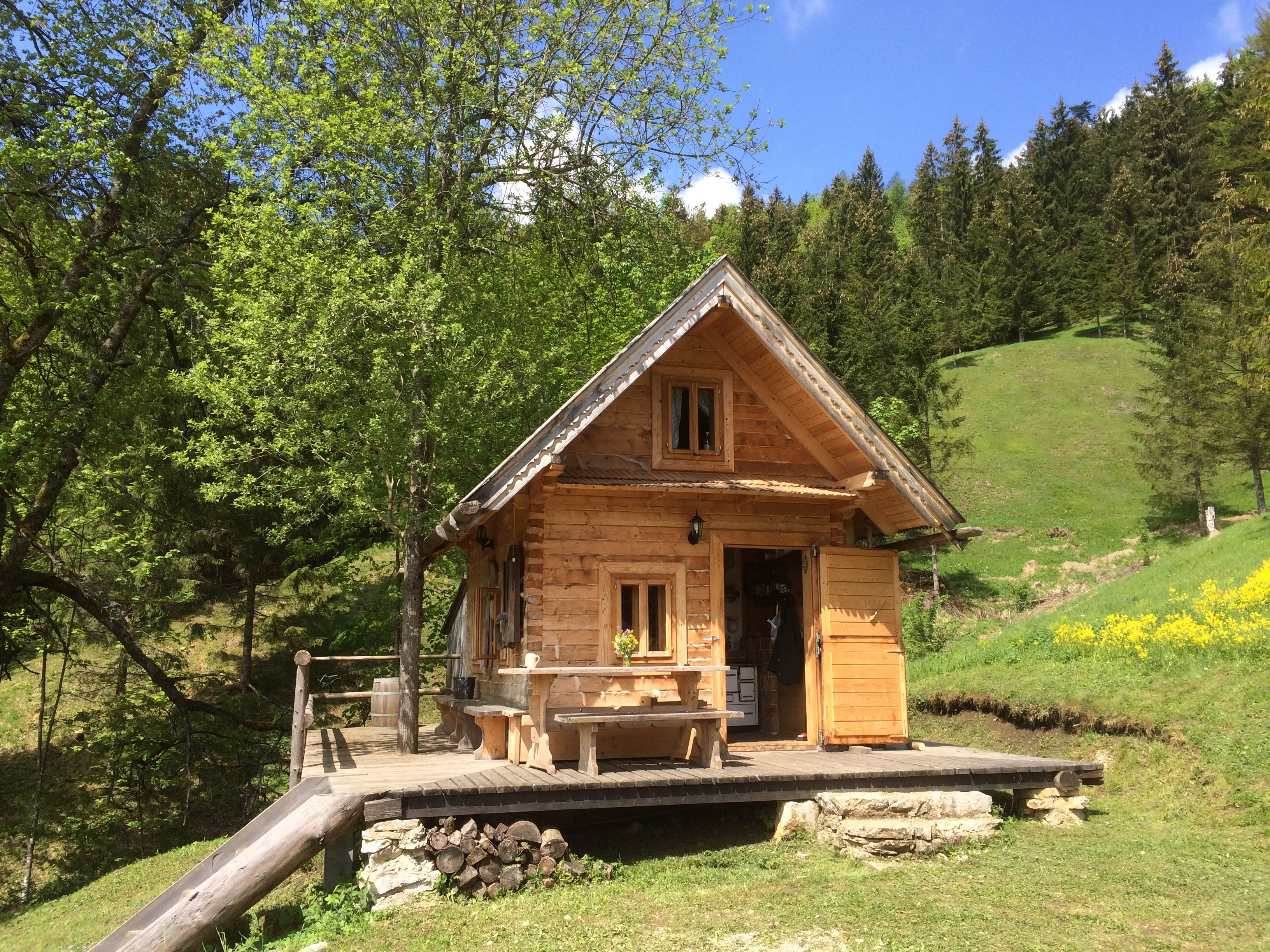 A small wooden hut in a green, wooded landscape with a blue sky.