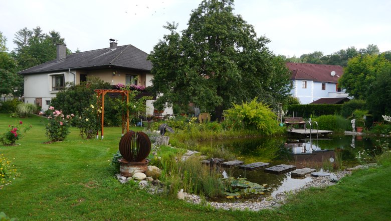 Garden with swimming biotope, © fbeck A garden with a swimming pool, surrounded by plants and a house in the background.