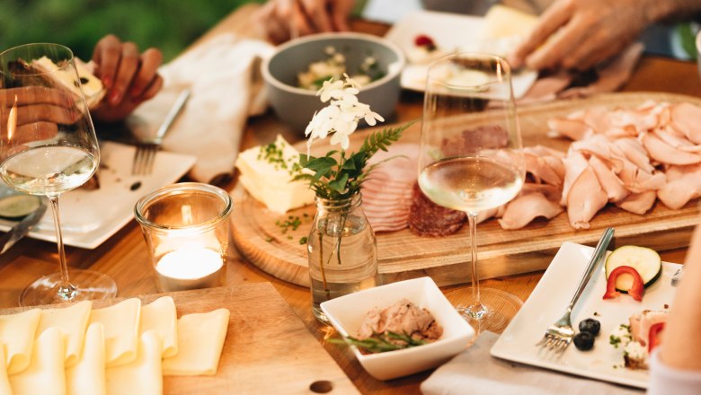 A table laid with bread, cheese, cold cuts and glasses of wine.