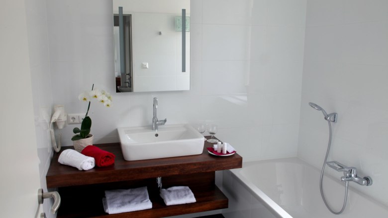 Modern bathroom with washbasin, mirror, bathtub and towels.