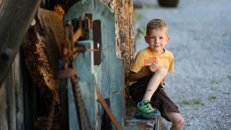 A boy sits on a wooden bench and holds the Wilde Wunder Card in his hand.