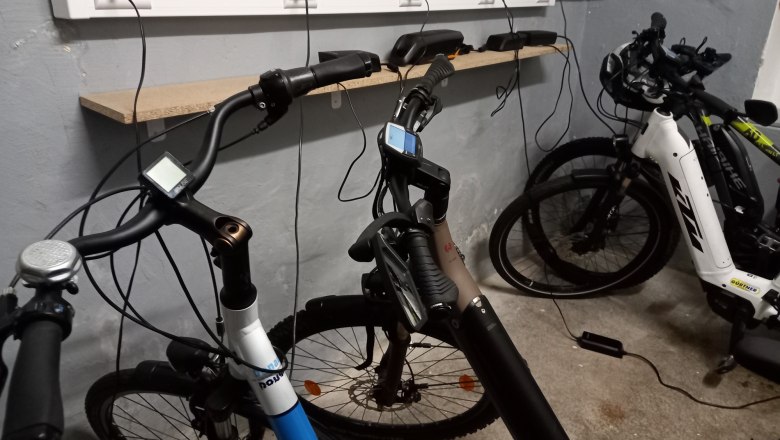 Three e-bikes in a garage being charged at a power strip.