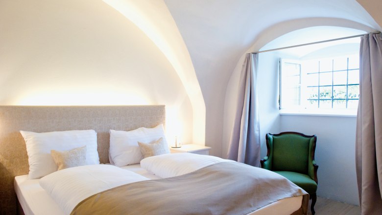 Cozy bedroom with double bed, green armchair and vaulted ceiling.