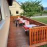 Wooden terrace with covered tables and chairs, surrounded by green landscape.