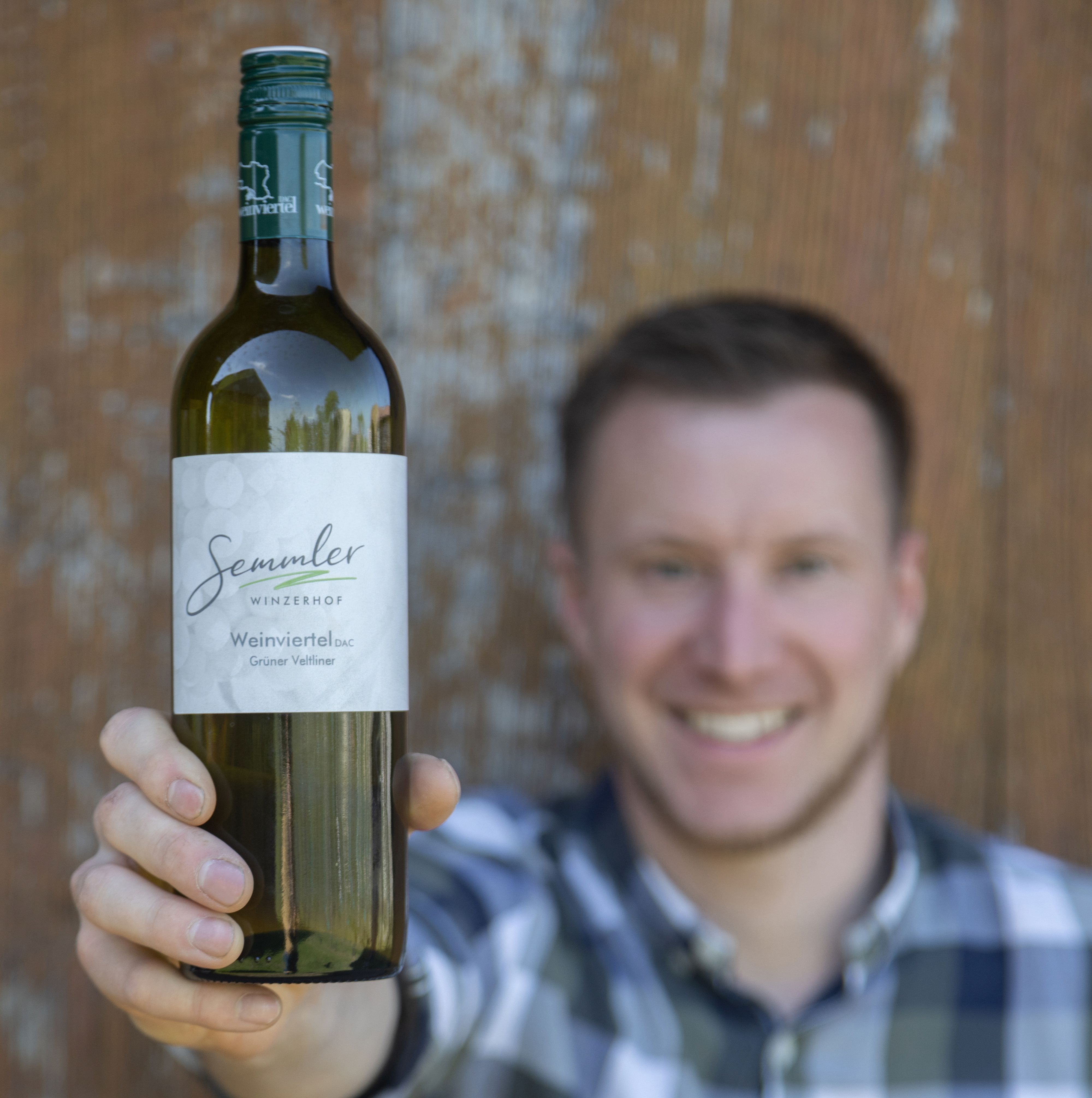 A man holds a bottle of wine from Winzerhof Semmler up to the camera.