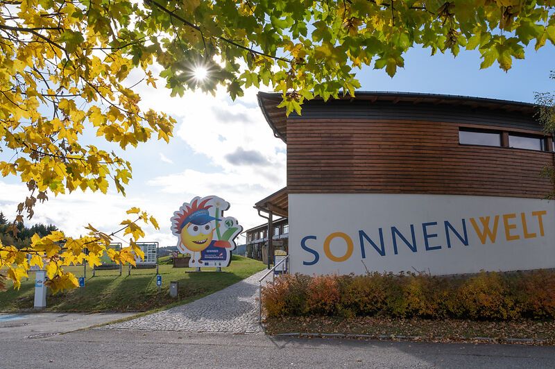 Entrance to SONNENWELT Großschönau with autumnal trees and sunshine.