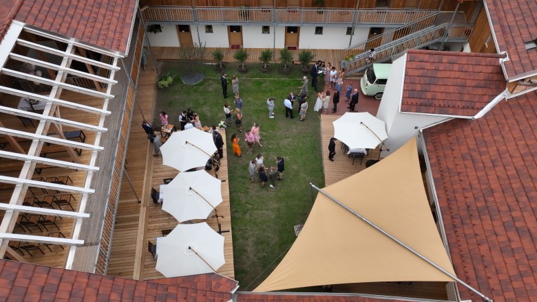 Bird's eye view of the inner courtyard with green lawn, white parasols and guests at a reception.