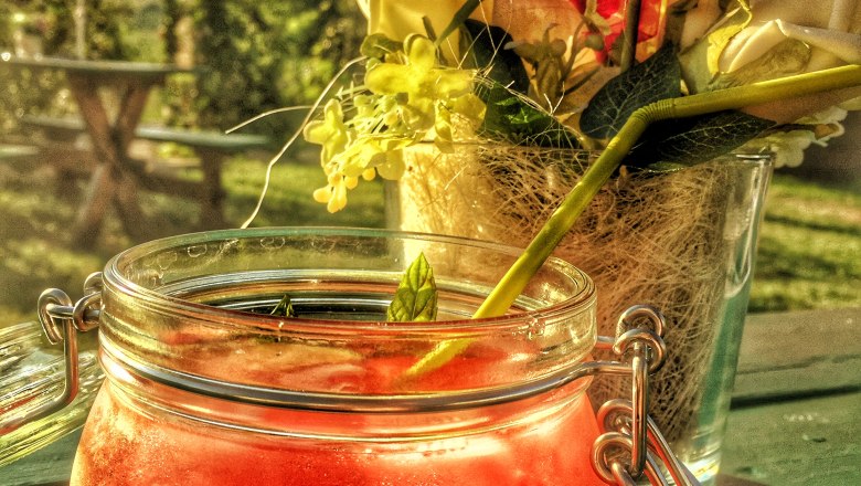 A red drink in a glass with a swing top, next to it a bouquet of flowers on an outdoor table.