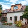 Rustic house with tiled roof and wooden cladding, surrounded by plants and cobblestones.