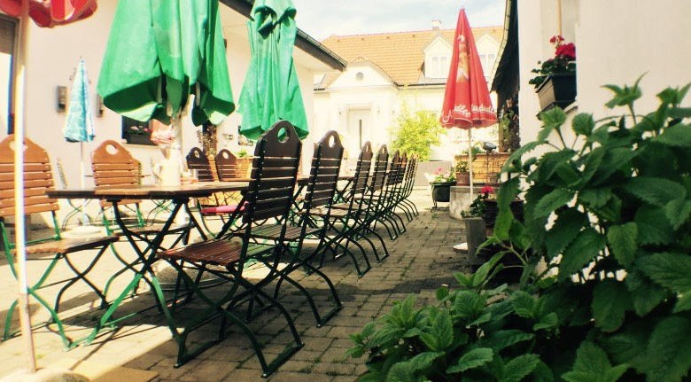 An empty guest garden with wooden tables and chairs, surrounded by green parasols and plants.