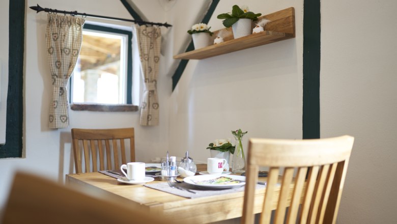 A cozy breakfast room with a wooden table, chairs and decorative plants on a shelf.