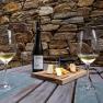 Two wine glasses and a bottle of wine on a wooden table with a cheese board, in front of a stone wall.