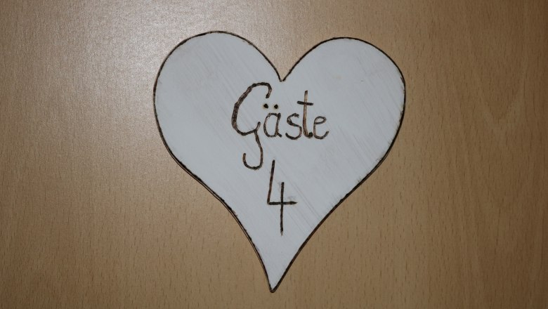 Wooden sign in the shape of a heart with the inscription 'Gäste 4'.