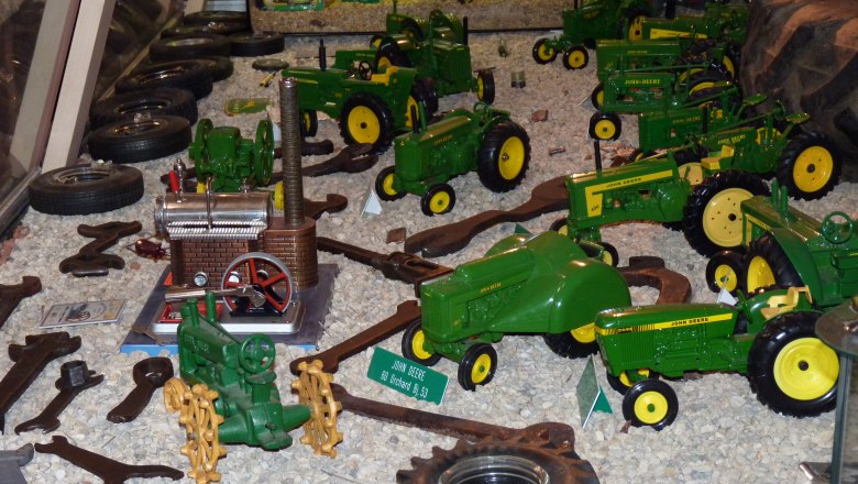 Collection of model tractors exhibited on gravel.