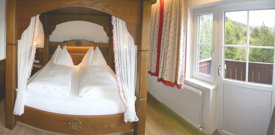 Cozy bedroom with four-poster bed and balcony view of the countryside.