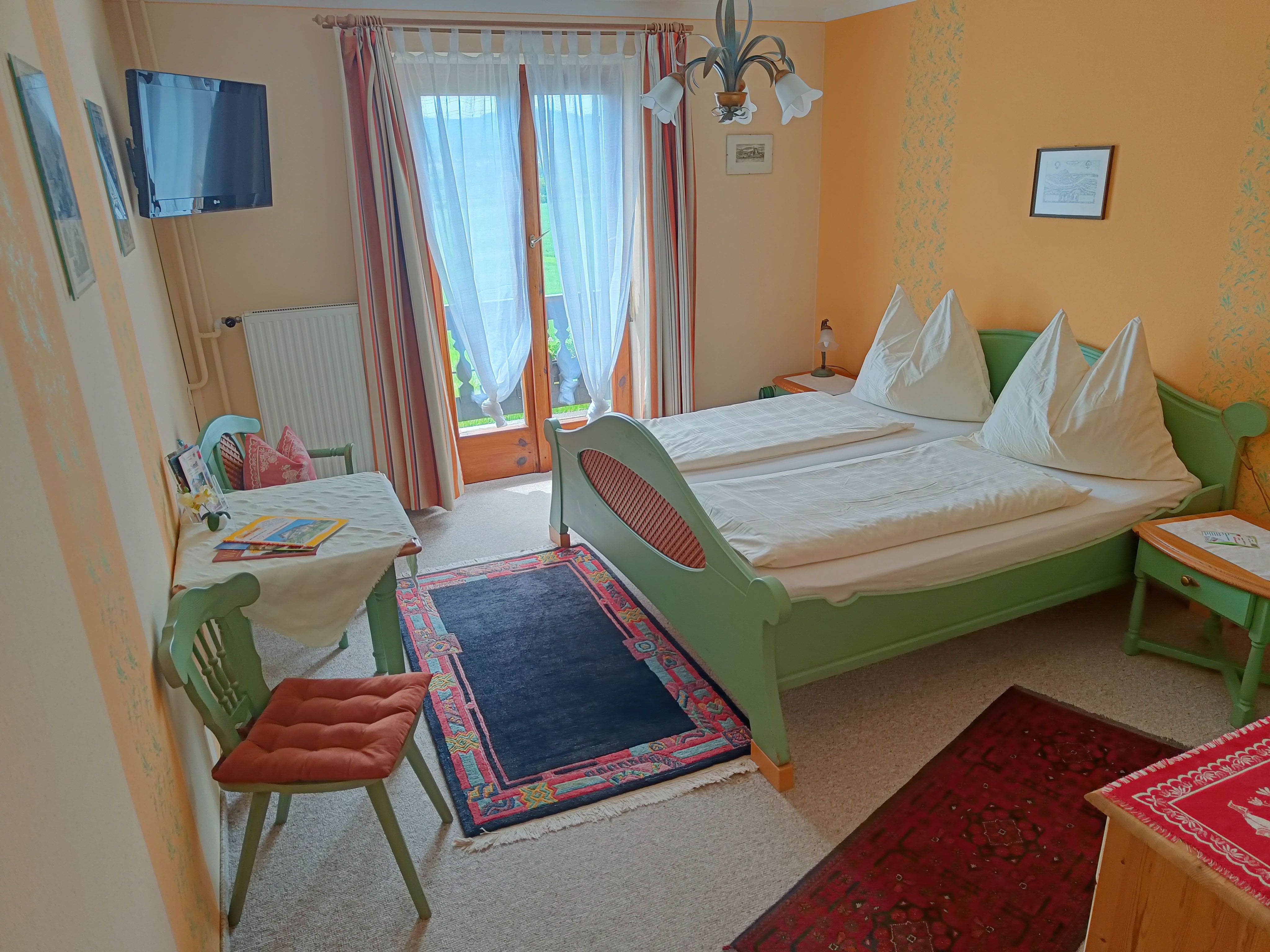 Room with green double bed and table with chair