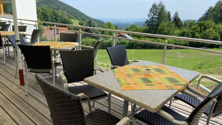 Terrace with tables and chairs, view of green hills and trees in the background.