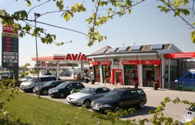 Petrol station with AVIA logo and several parked cars in the foreground.