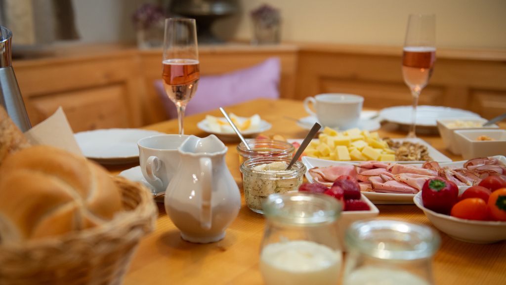 Breakfast table with bread rolls, cold cuts, cheese, champagne glasses and yogurt.