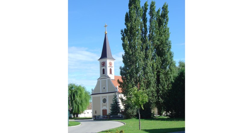A church with a tower and clock against a blue sky, surrounded by trees.