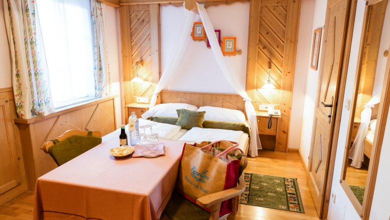 Cozy double room with wooden furniture, a table with drinks and snacks, and a bed with a canopy.