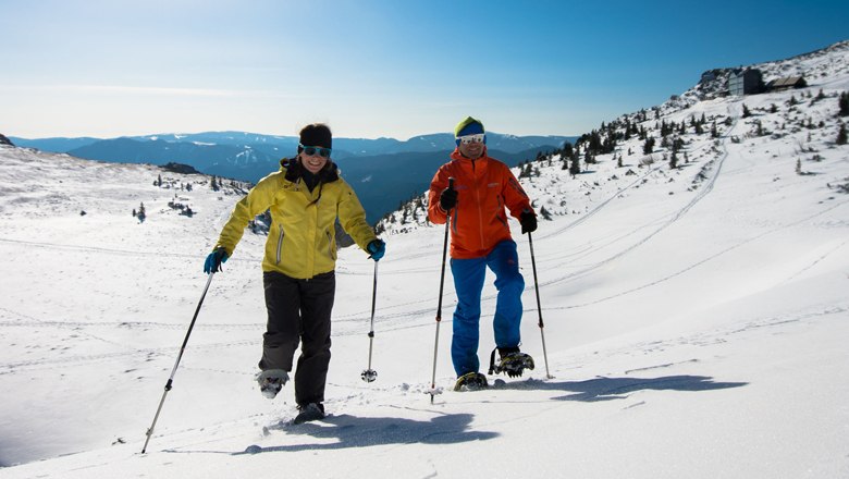 Two people snowshoeing in a snowy mountain landscape.