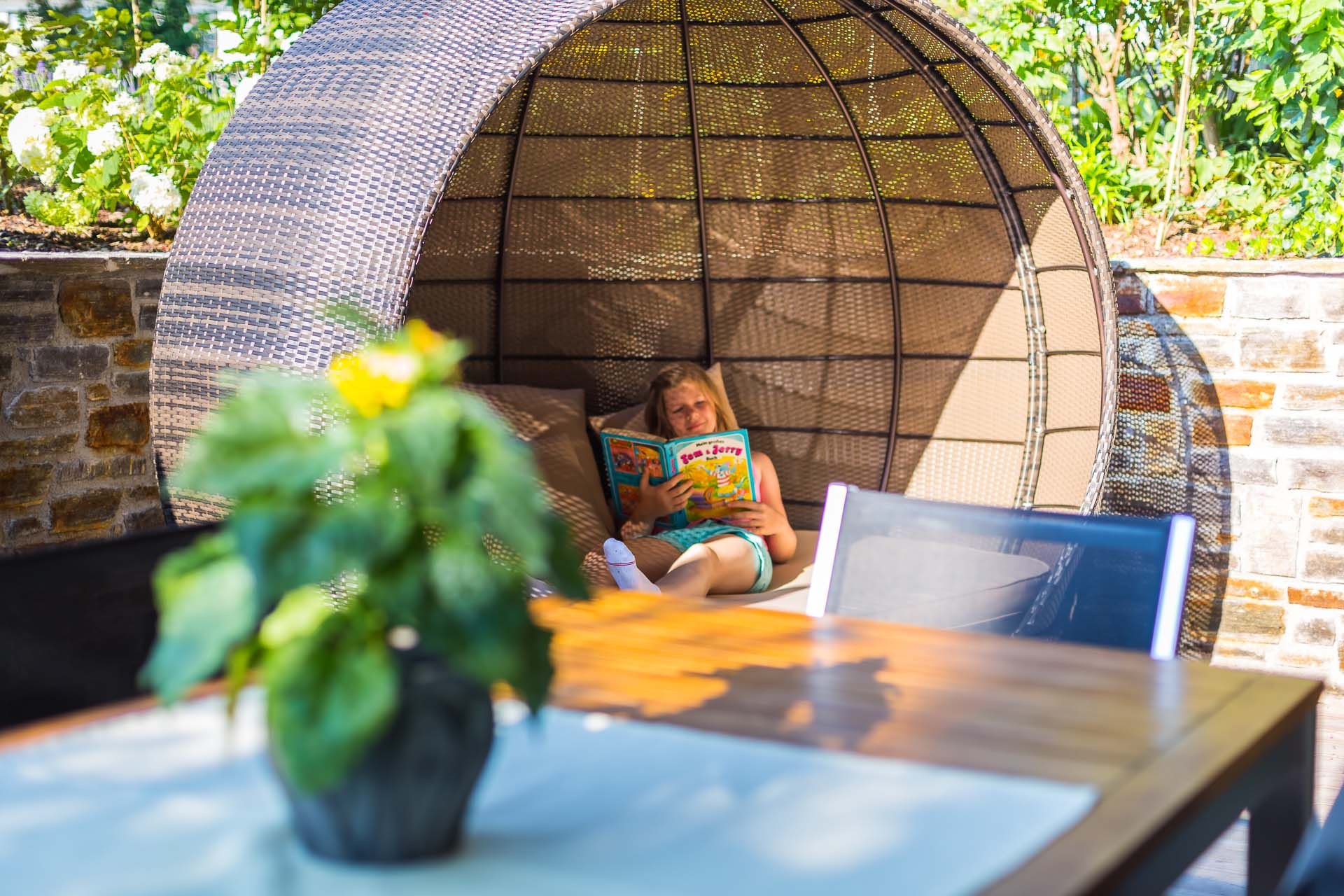 Person reads a book in a round, woven seat outside.