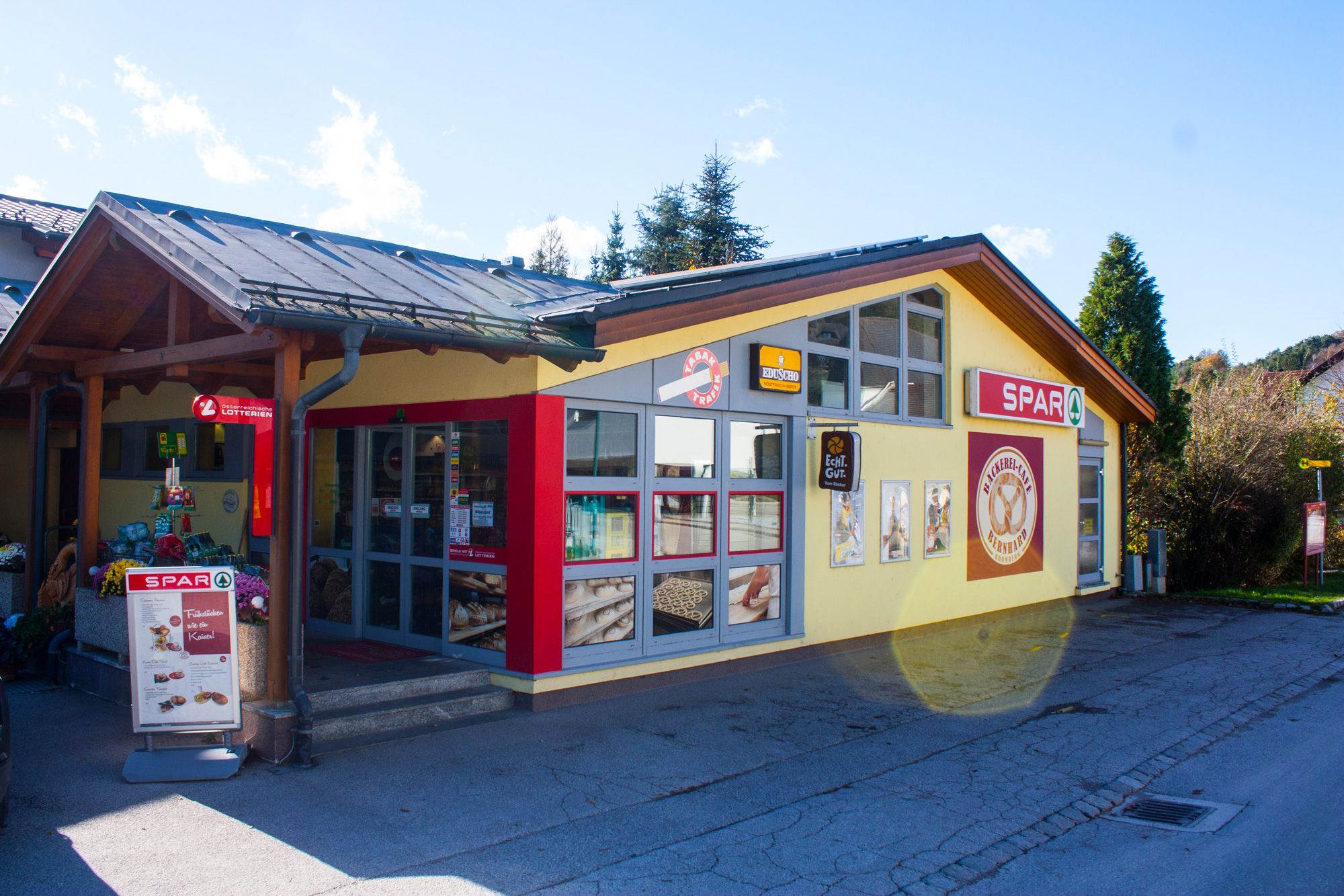 Exterior view of a bakery and a Spar supermarket in the sunshine.