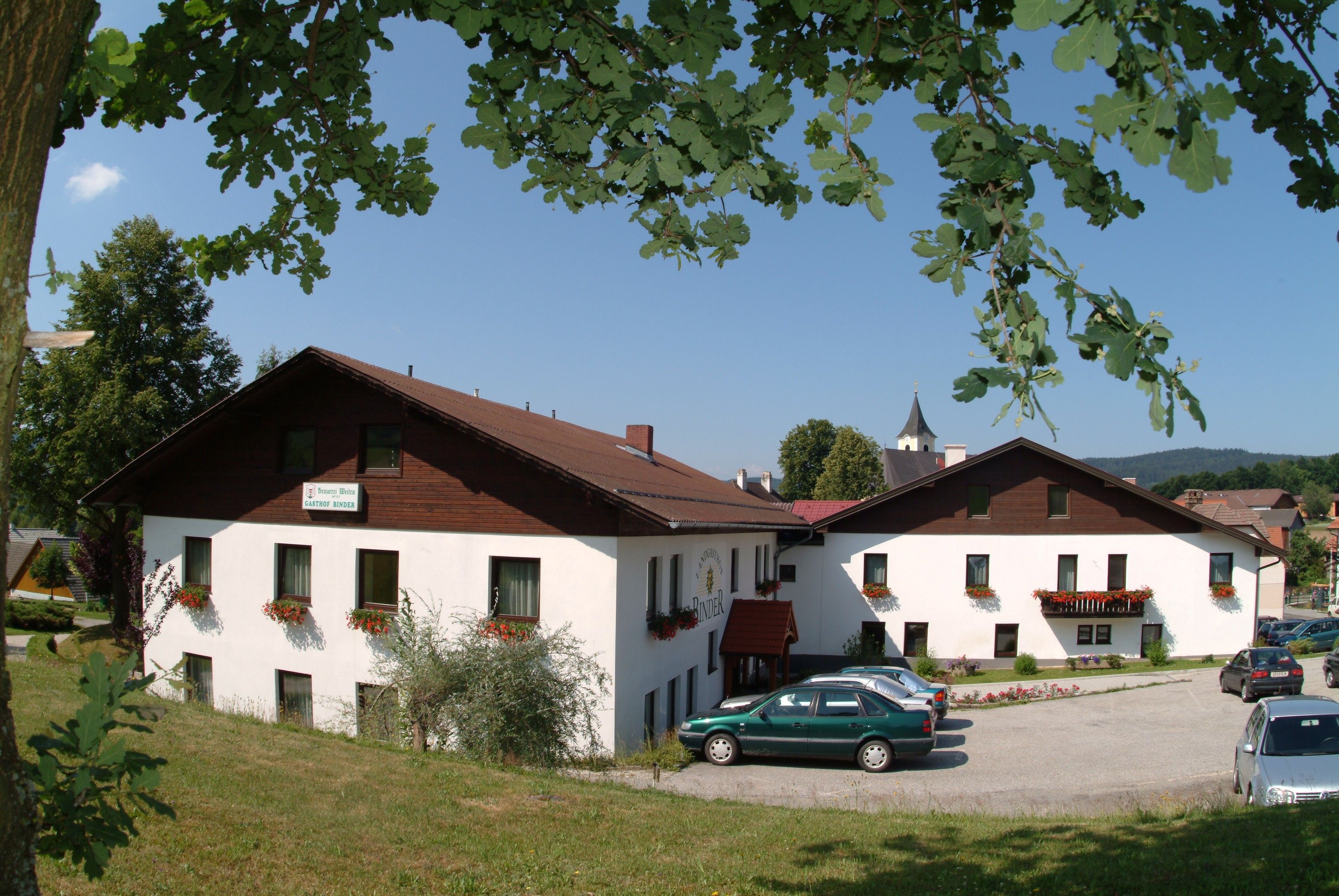 A country inn with white walls and a brown roof, surrounded by trees and cars in a parking lot.