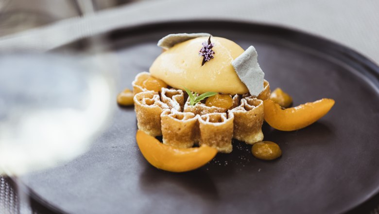 An artfully arranged waffle with apricot sorbet and decorative fruit on a black plate.