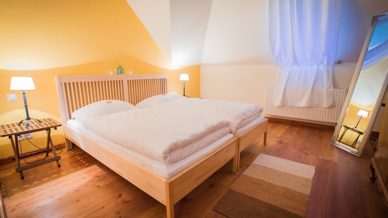 Cozy bedroom with double bed, wooden floor, yellow wall and large mirror.