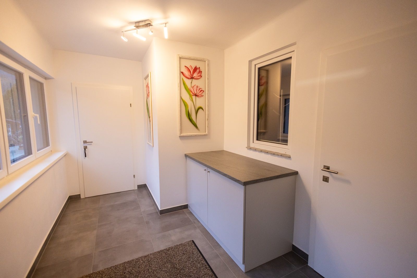 Modern anteroom with white walls, gray floor, a cupboard and flower pictures on the wall.